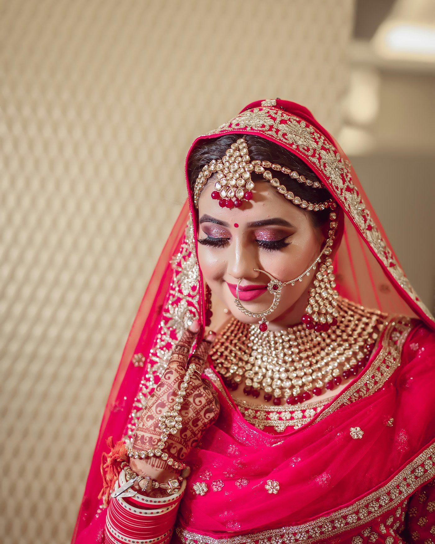 South Asian bride in red bridal attire with intricate gold jewelry and henna