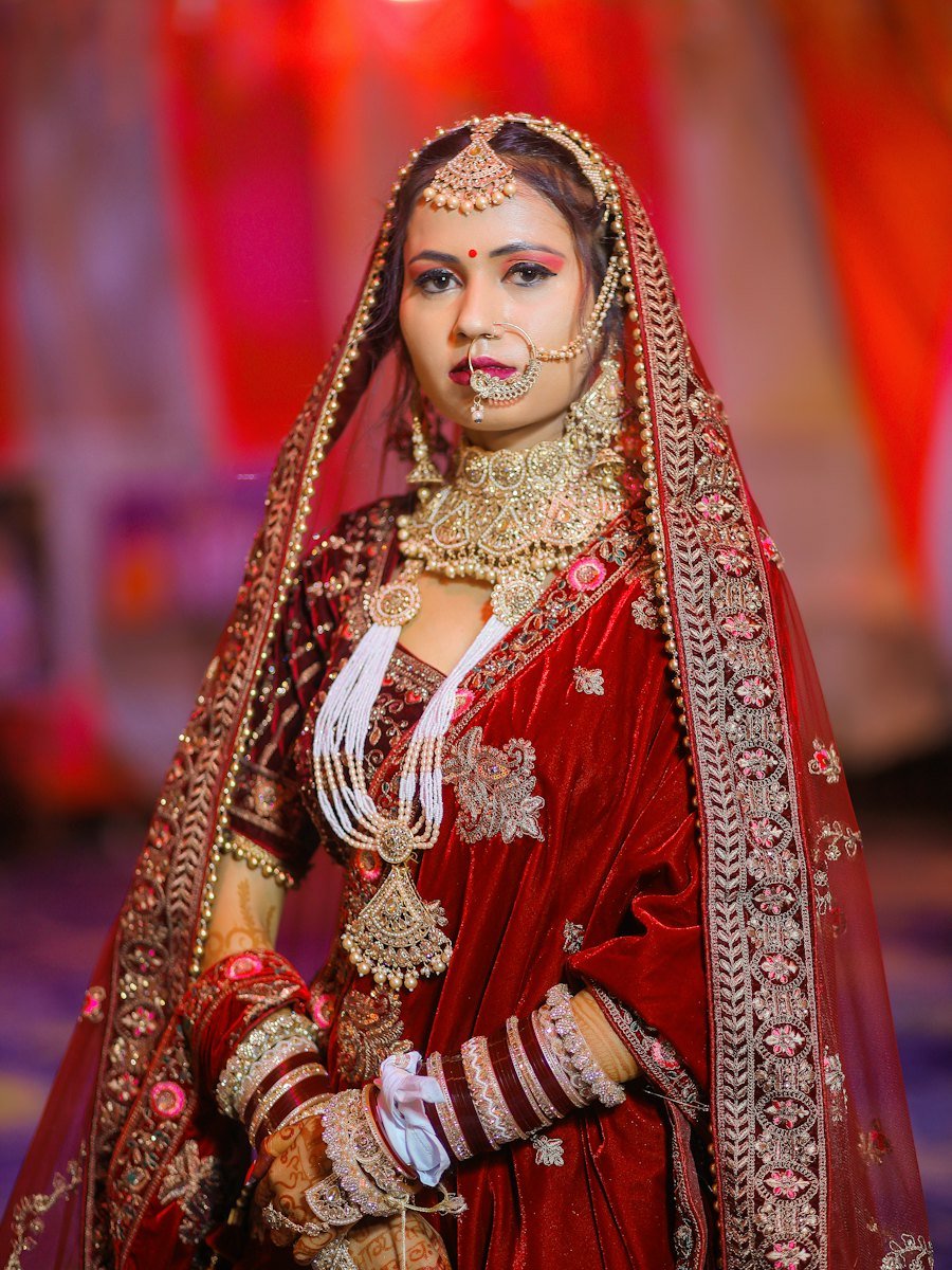 Bride in a red velvet lehenga wearing layered gold bridal jewelry