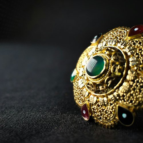 Ornate gold ring set with colored gemstones on a dark surface