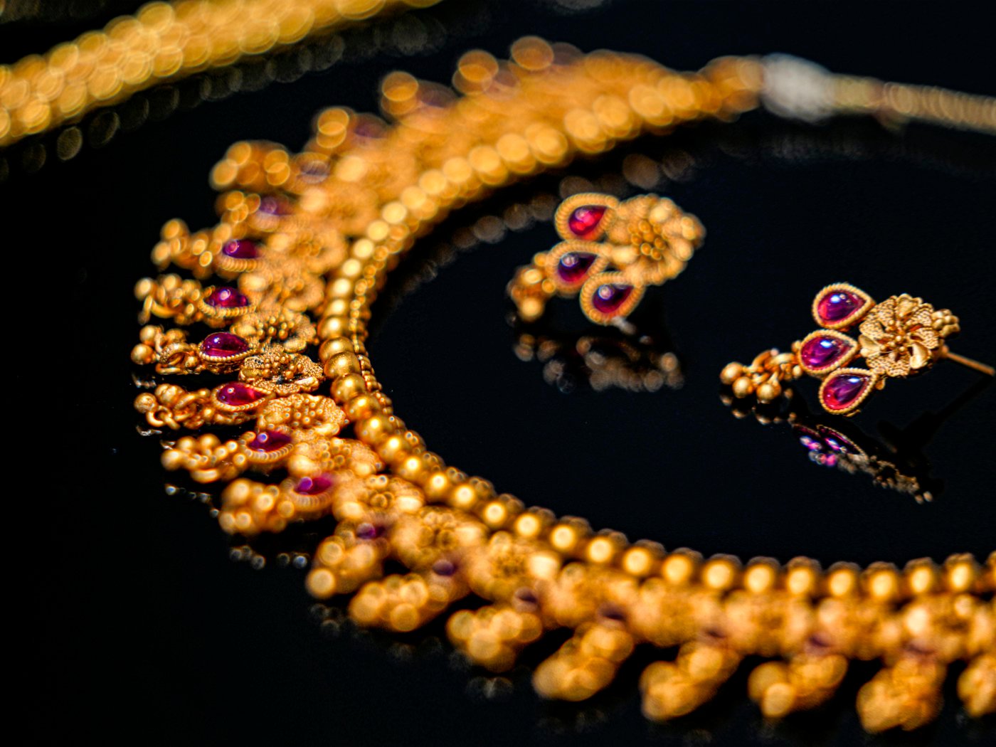 Ornate 22kt gold necklace with ruby-red accents and matching earrings on a dark background