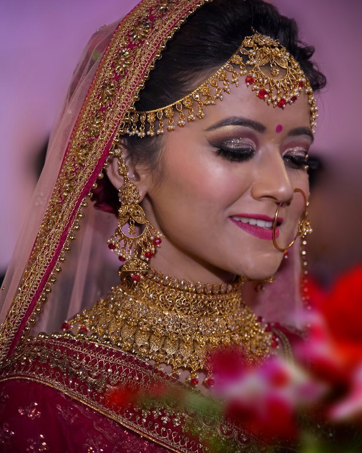 Bride in red bridal attire with an ornate gold necklace, earrings and veil