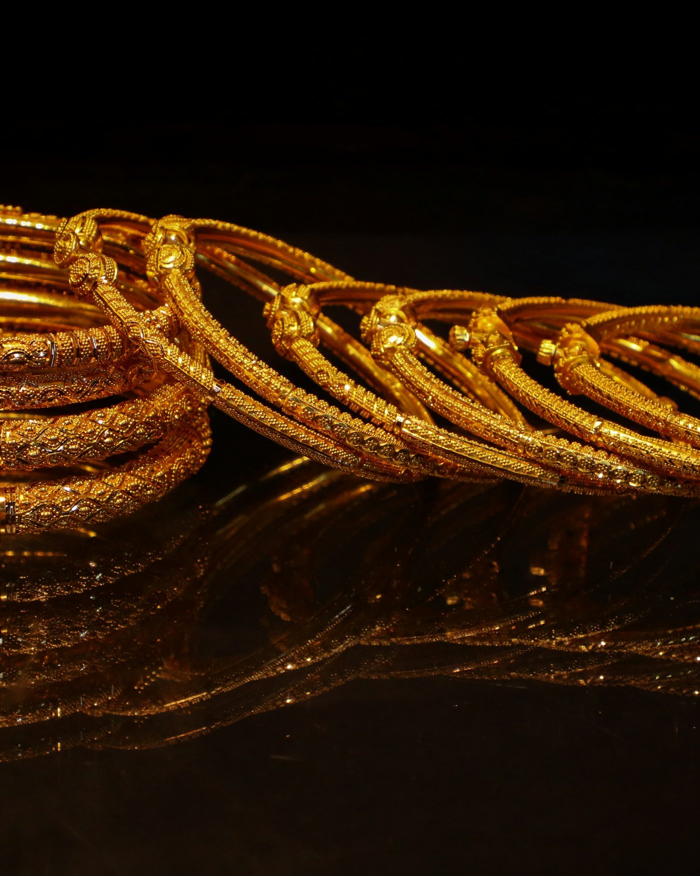 A stack of ornate 22kt gold bangles with detailed engraving on a dark surface