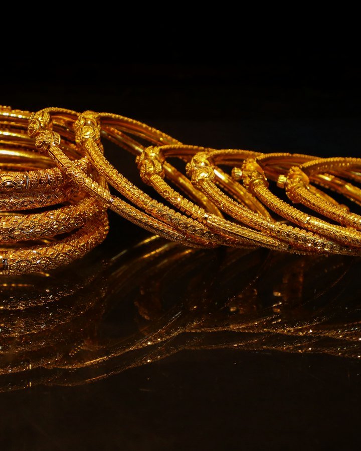 A stack of ornate 22kt gold bangles on a dark surface