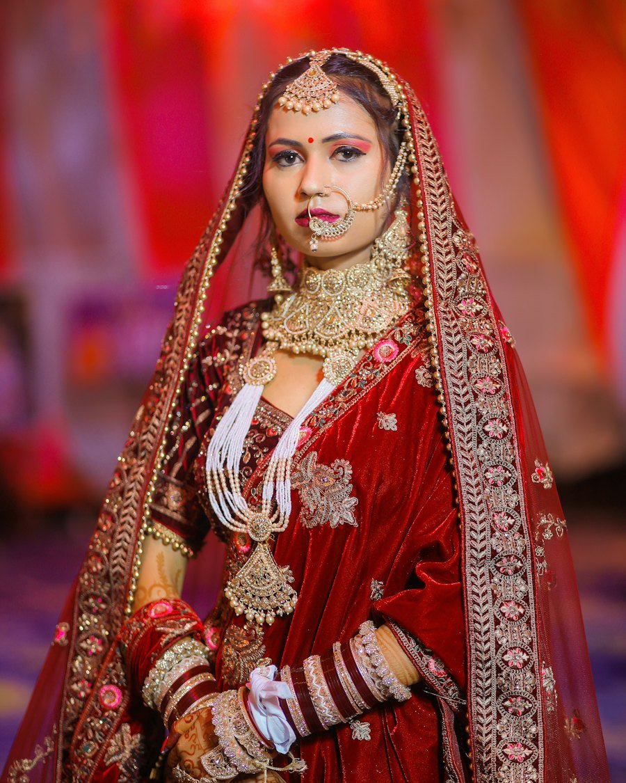 Bride in a red velvet lehenga wearing layered gold bridal jewelry