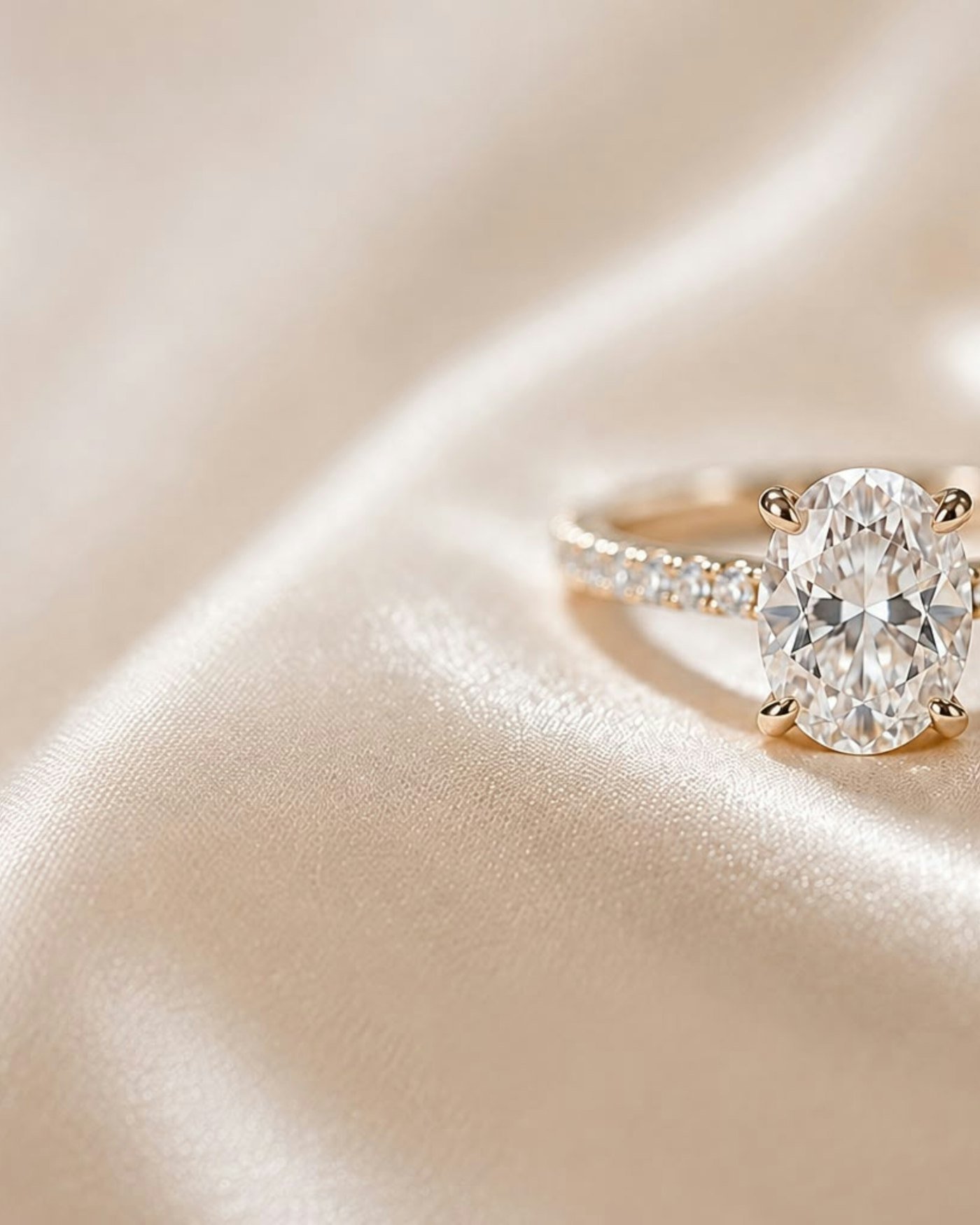 Oval diamond engagement ring with a gold band resting on champagne silk