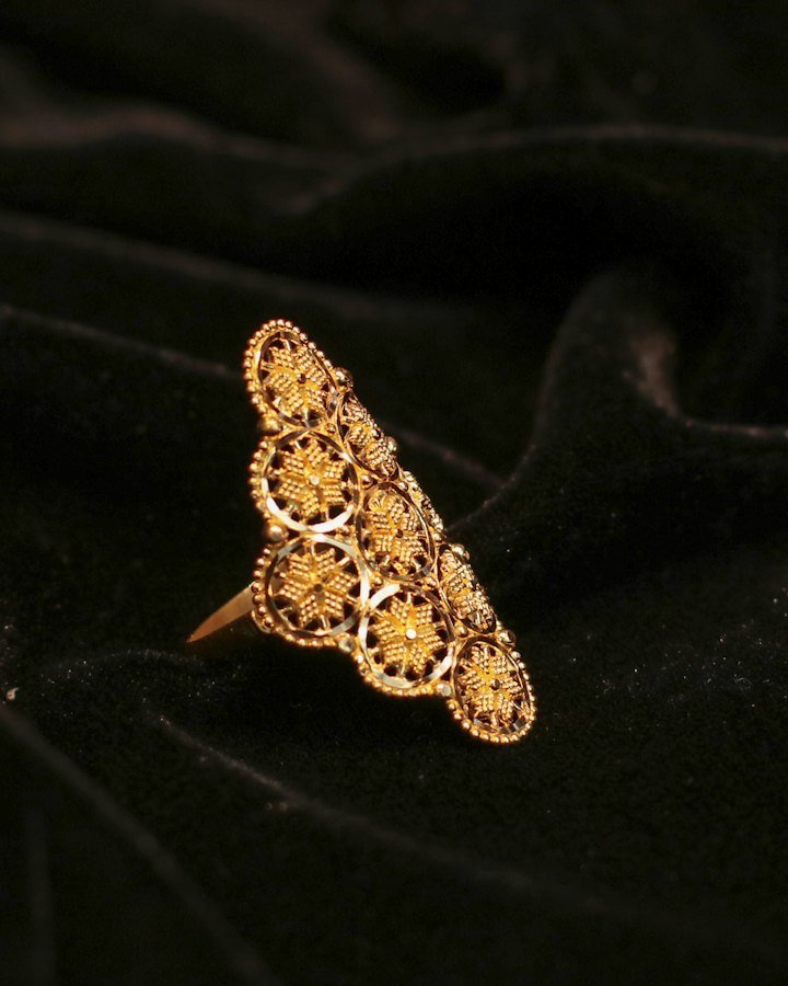 Ornate gold ring with intricate filigree on black velvet